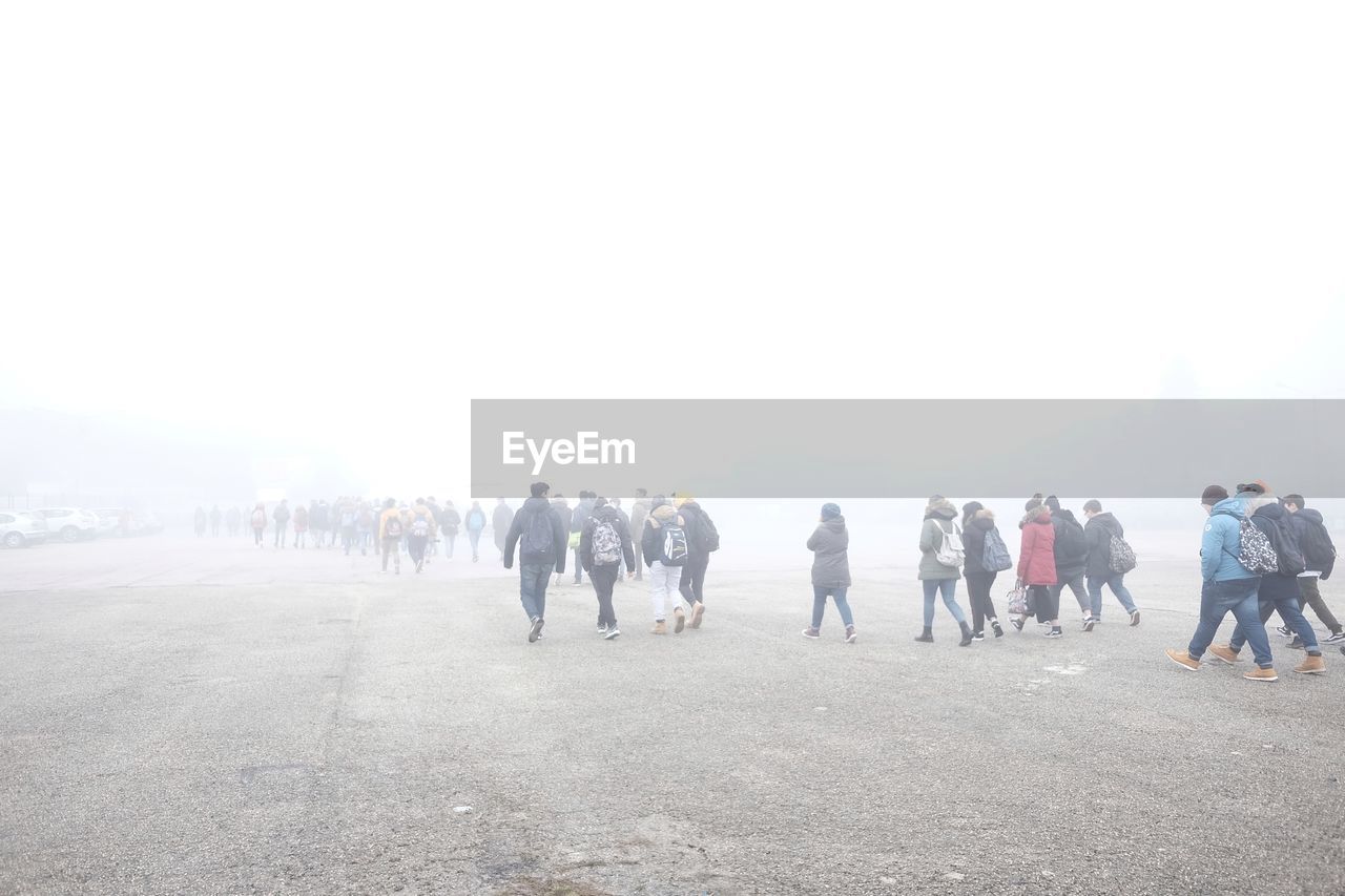 People walking on road against sky during foggy weather