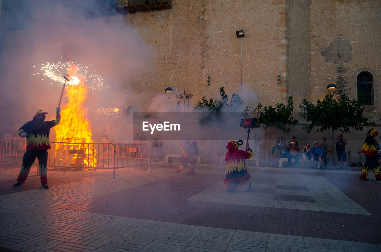 group of people, architecture, burning, city, fire, street, smoke, celebration, heat, tradition, building exterior, men, adult, night, nature, flame, crowd, large group of people, built structure, motion, religion, outdoors, arts culture and entertainment, sign, event
