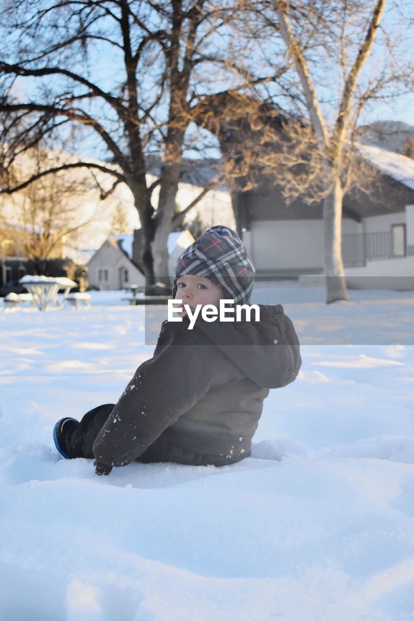 Cute baby boy sitting on snow covered field