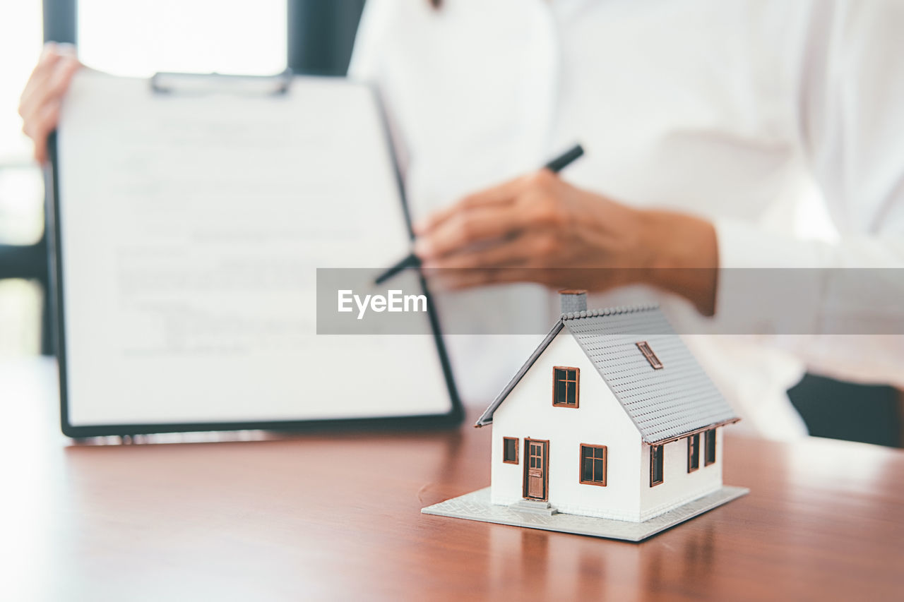 Midsection of businesswoman with model home on desk sitting in office