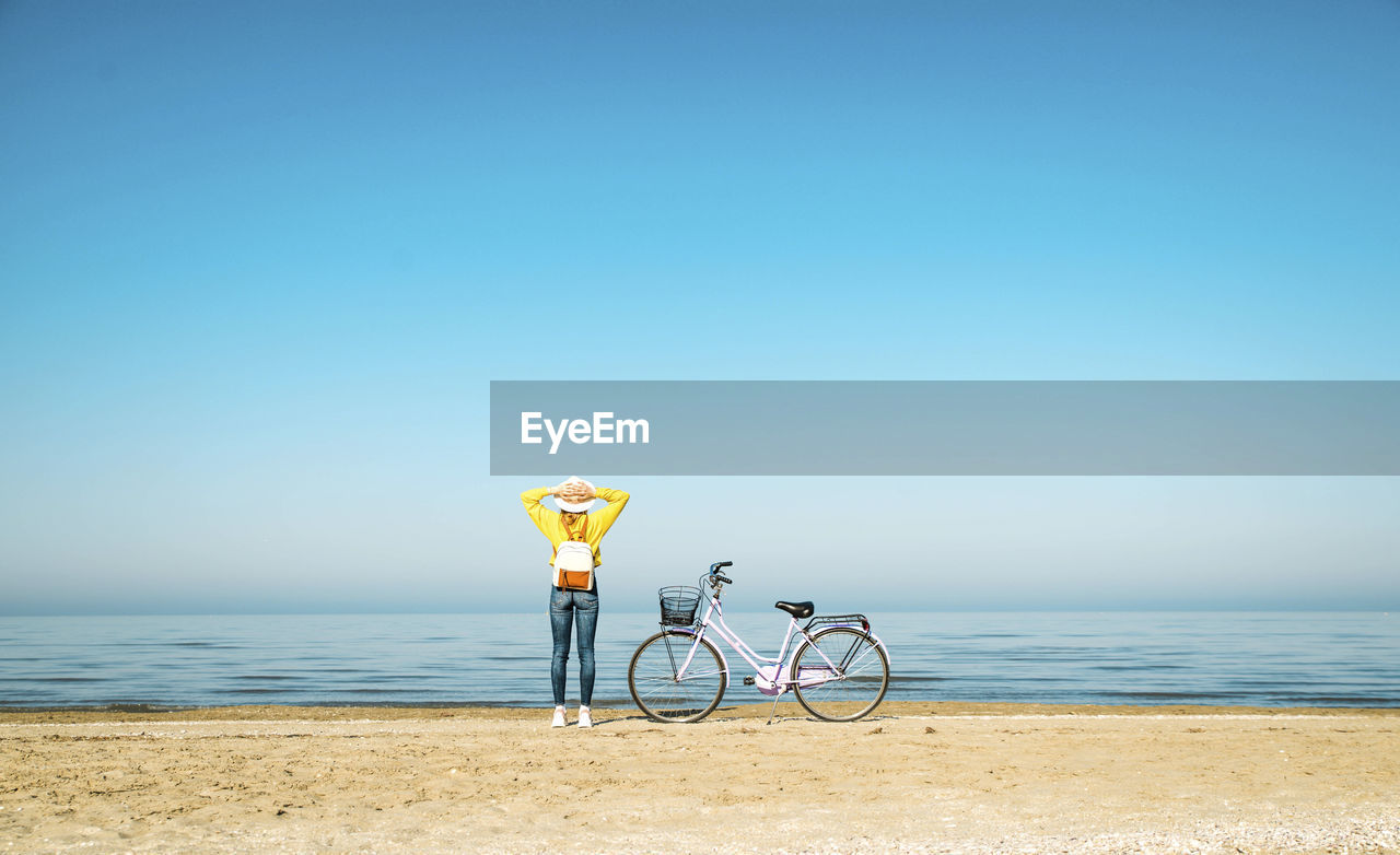 Woman looking at view while standing by bicycle on beach