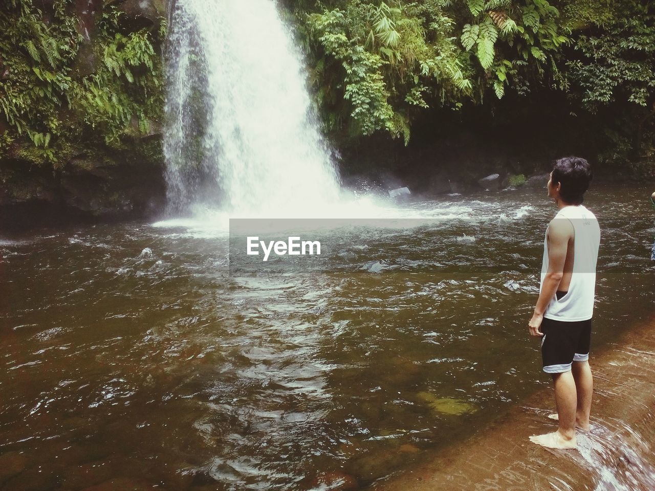 Full length of man looking at waterfall in forest