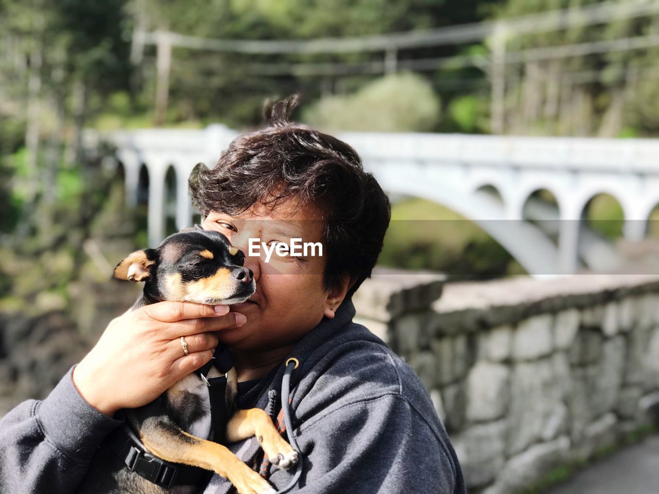 Portrait of woman holding puppy against bridge