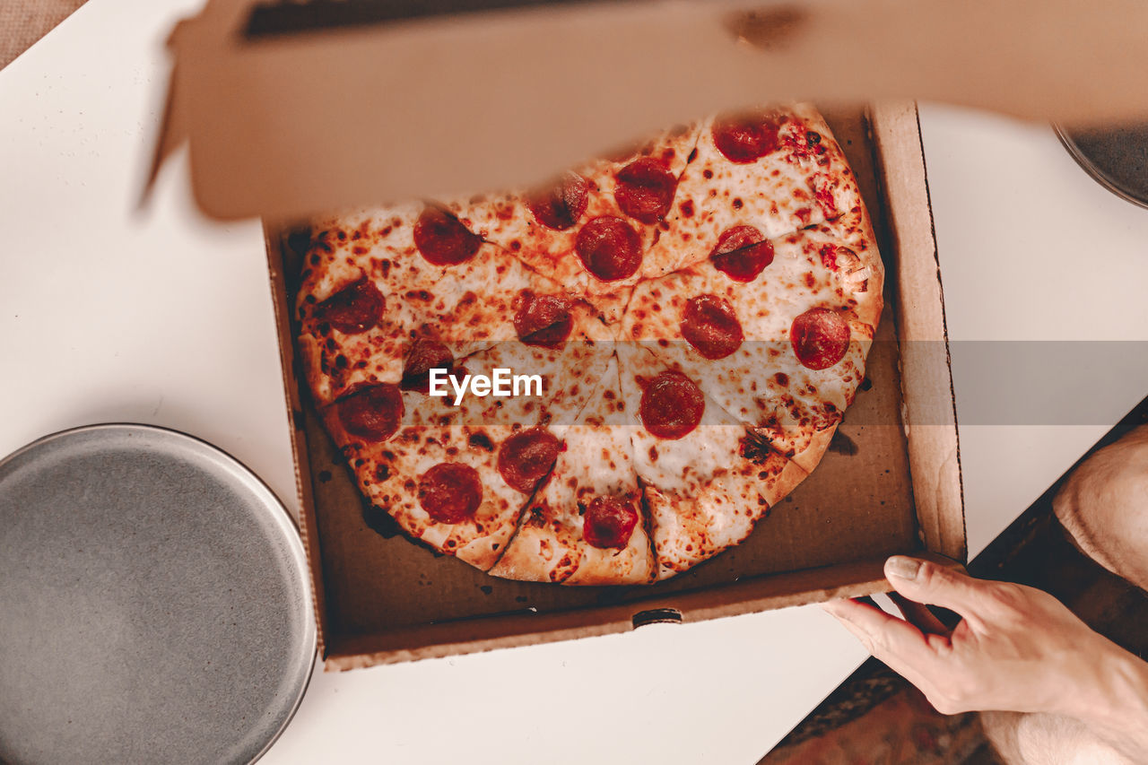 CLOSE-UP OF HAND HOLDING PIZZA IN BOX
