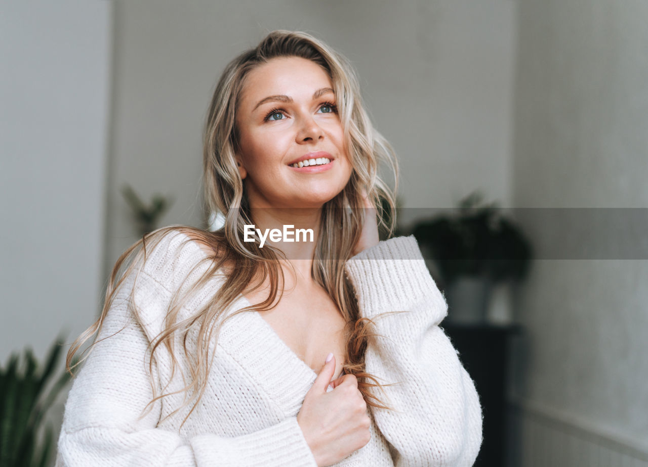 Blonde smiling woman 35 year plus clean fresh face and hands with long hair in cozy knitted cardigan 