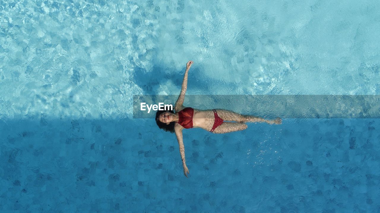 Woman in two peice swimming suit floating on blue swimming pool at the middle of light and shado