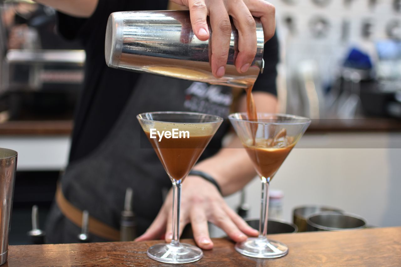 Midsection of bartender pouring cocktail in martini glass