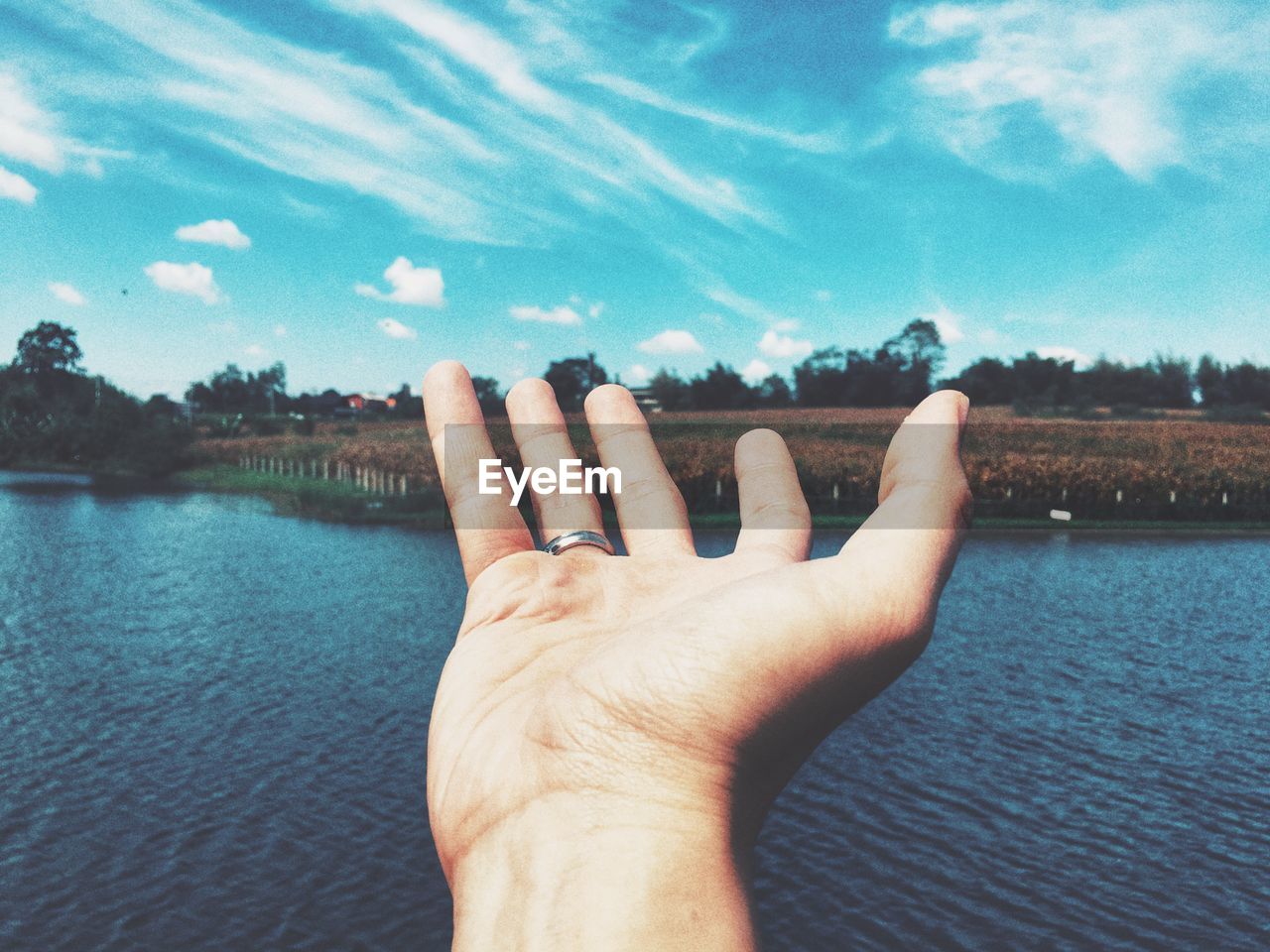 Close-up of hand over lake against sky