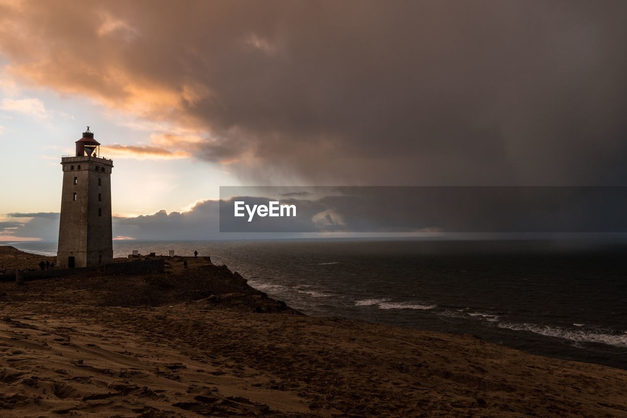 Lighthouse on beach by sea against sky