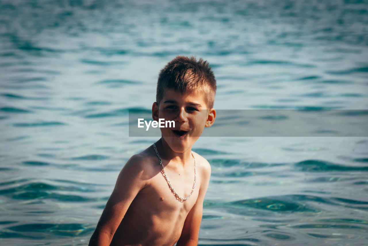 Portrait of shirtless boy with mouth open standing in sea