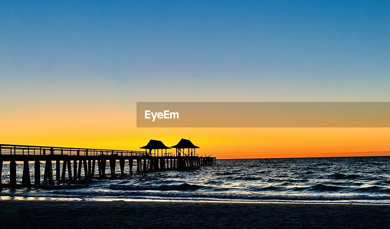 sky, sea, water, sunset, horizon, ocean, beauty in nature, beach, land, scenics - nature, horizon over water, nature, dusk, coast, tranquility, shore, tranquil scene, architecture, pier, wave, evening, built structure, idyllic, silhouette, no people, travel destinations, clear sky, orange color, copy space, outdoors, sunlight, sun, motion, body of water, seascape, travel, sand