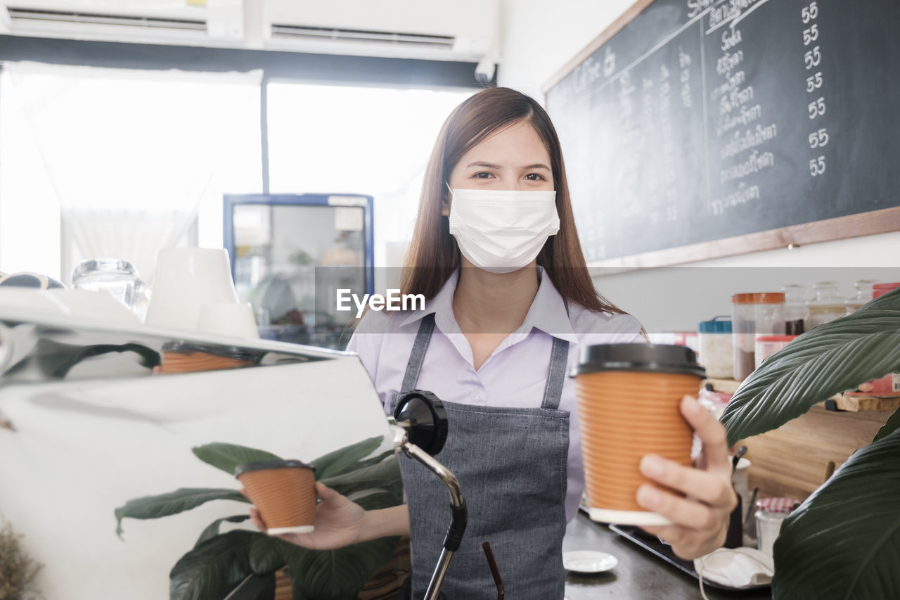 Portrait of barista holding coffee cup in cafe