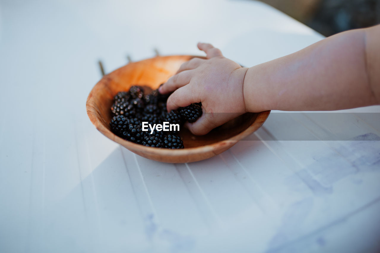 Cropped hand of baby picking blackberries from plate at table