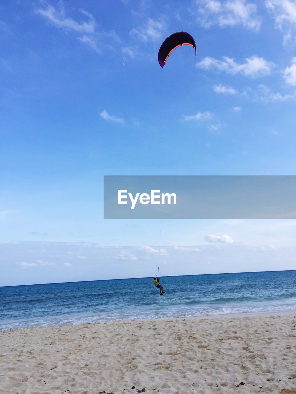 WOMAN FLYING OVER BEACH AGAINST SKY