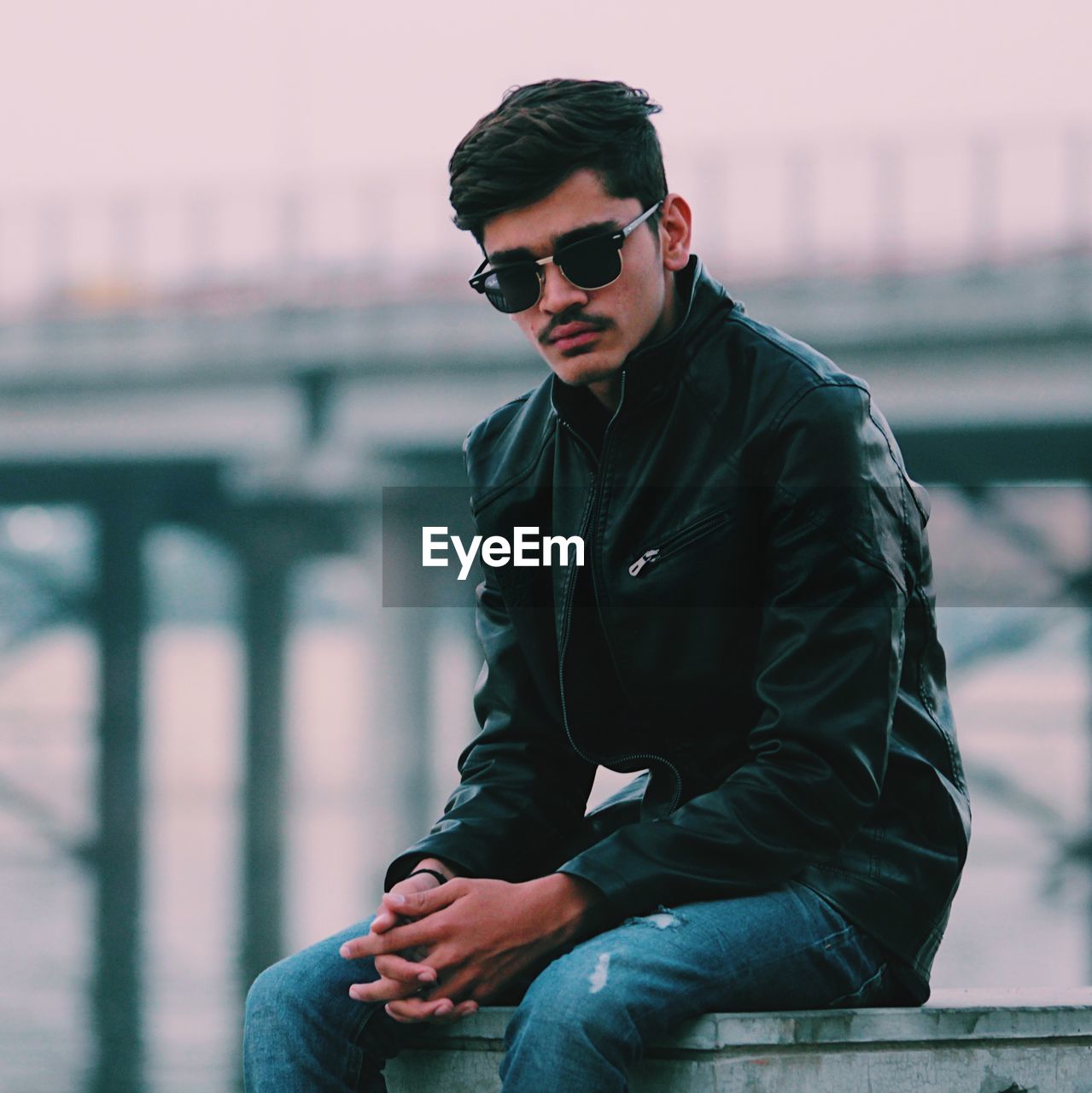 Fashionable man wearing sunglasses sitting against bridge