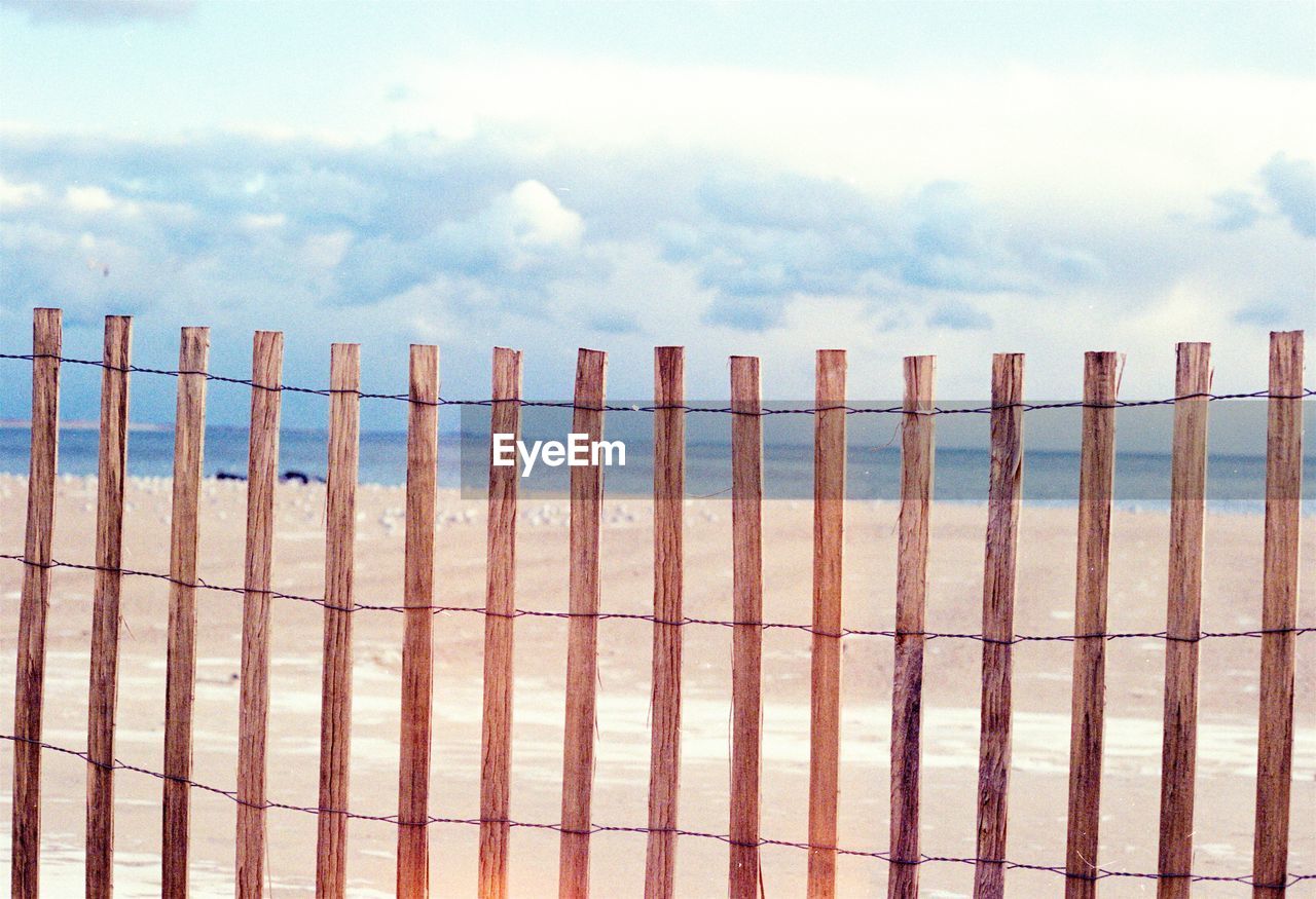 Wooden fence at beach against cloudy sky