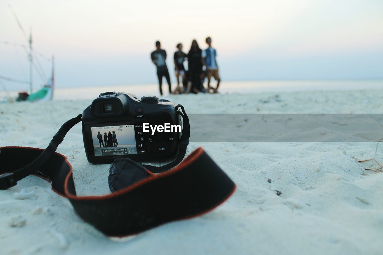 Camera at beach against friends during sunset