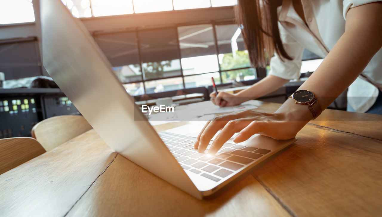 Midsection of woman using laptop on desk 