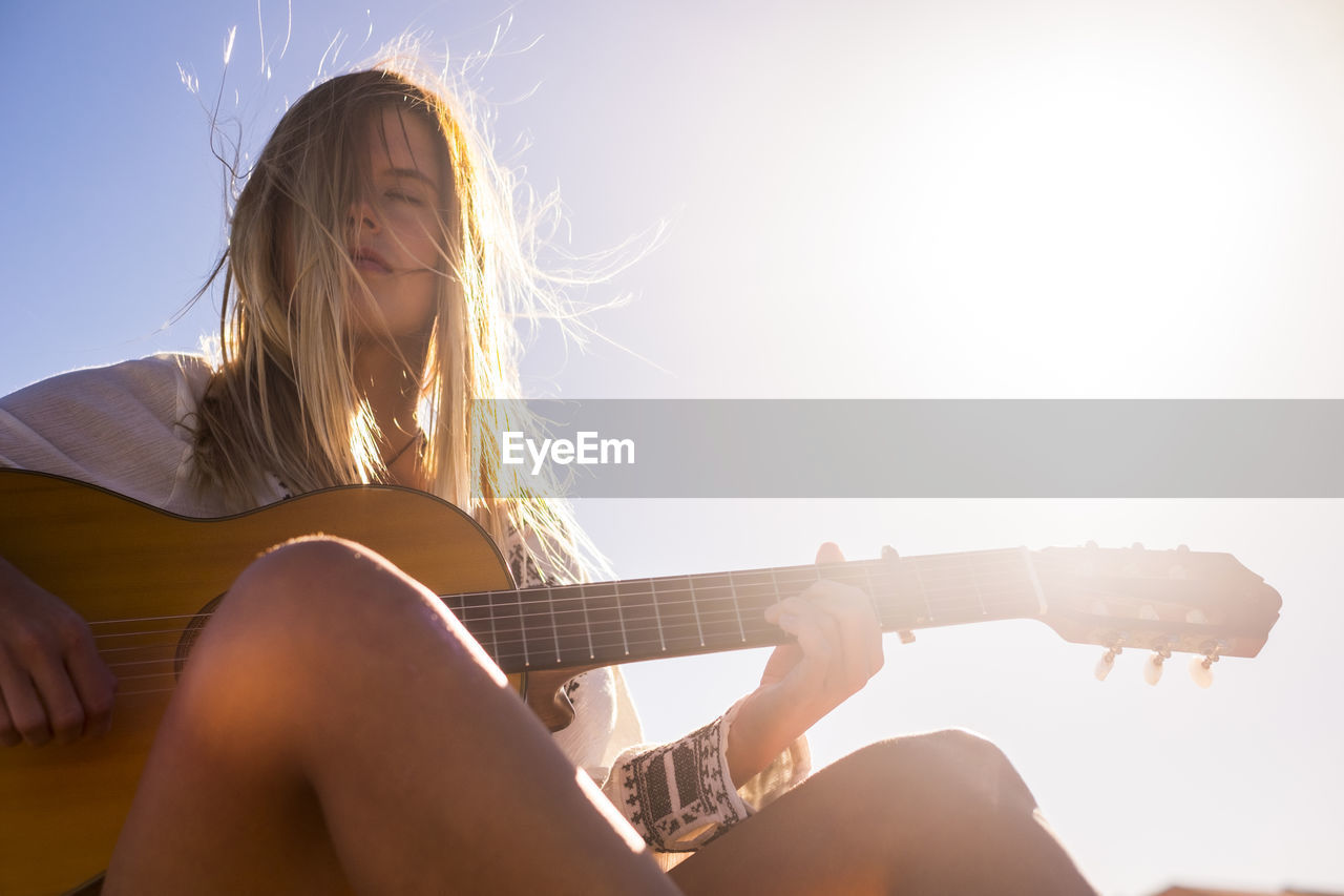 Close-up of woman playing guitar against sky on sunny day