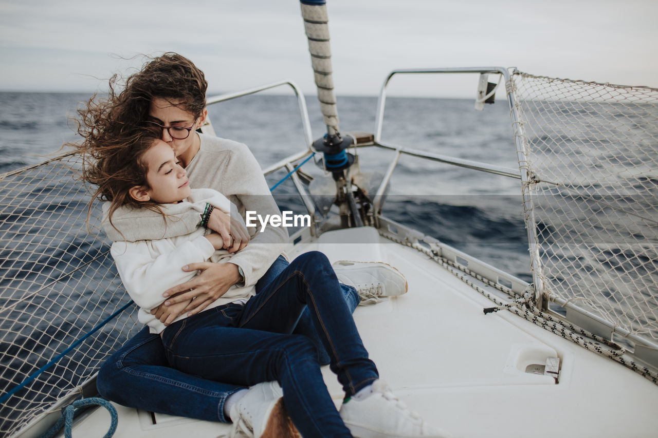 Mother kissing daughter while sitting on sailboat