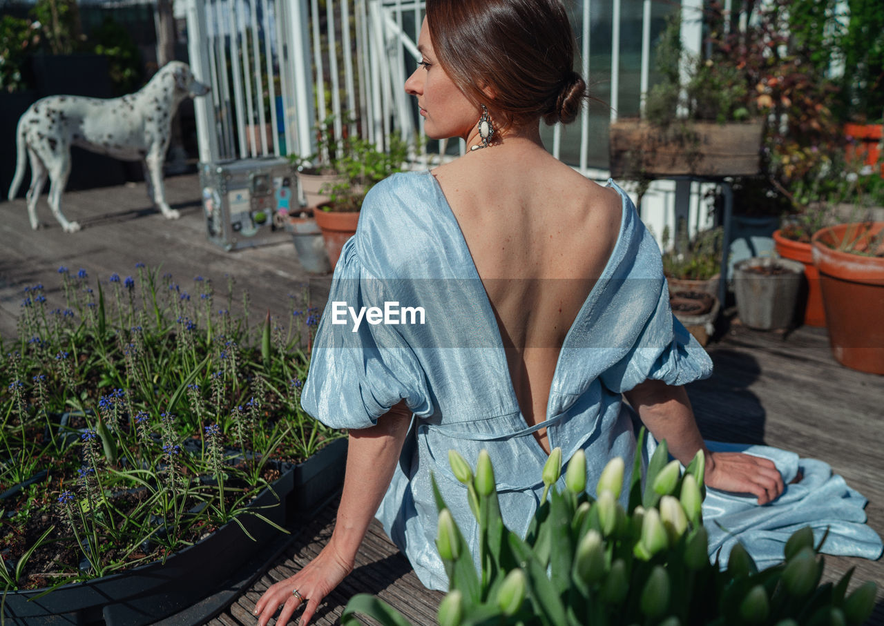 Rear view of woman sitting by potted plants outdoors