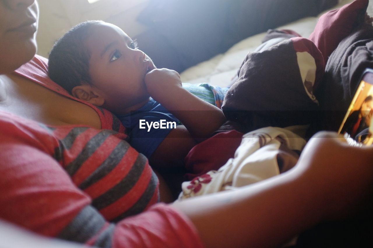 Tilt shot of boy lying on mother at home