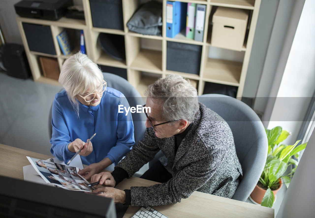 Two senior colleagues working together at desk in office discussing photos