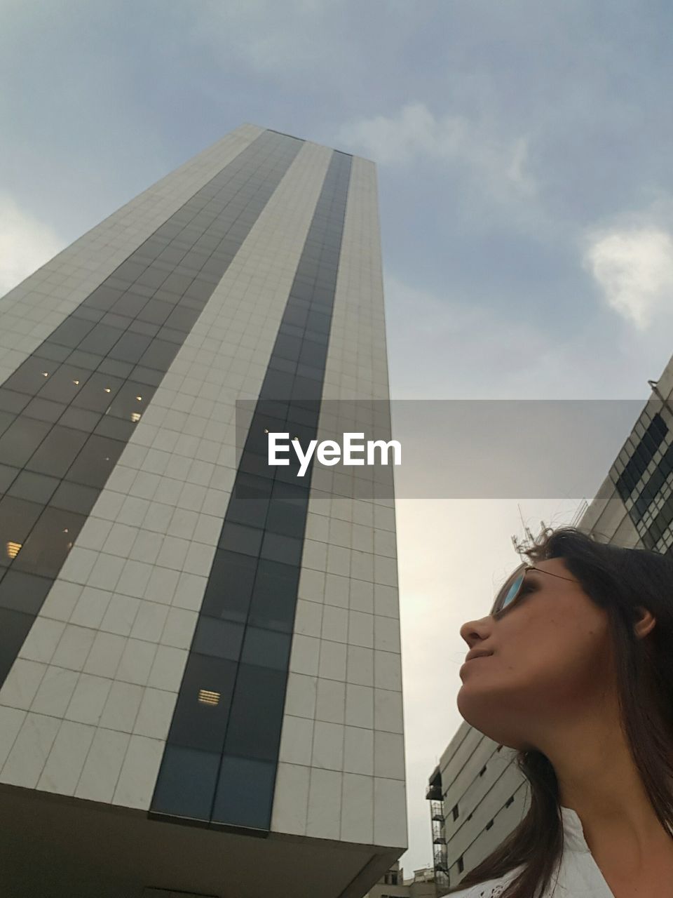 LOW ANGLE VIEW OF WOMAN WITH SKYSCRAPERS AGAINST SKY