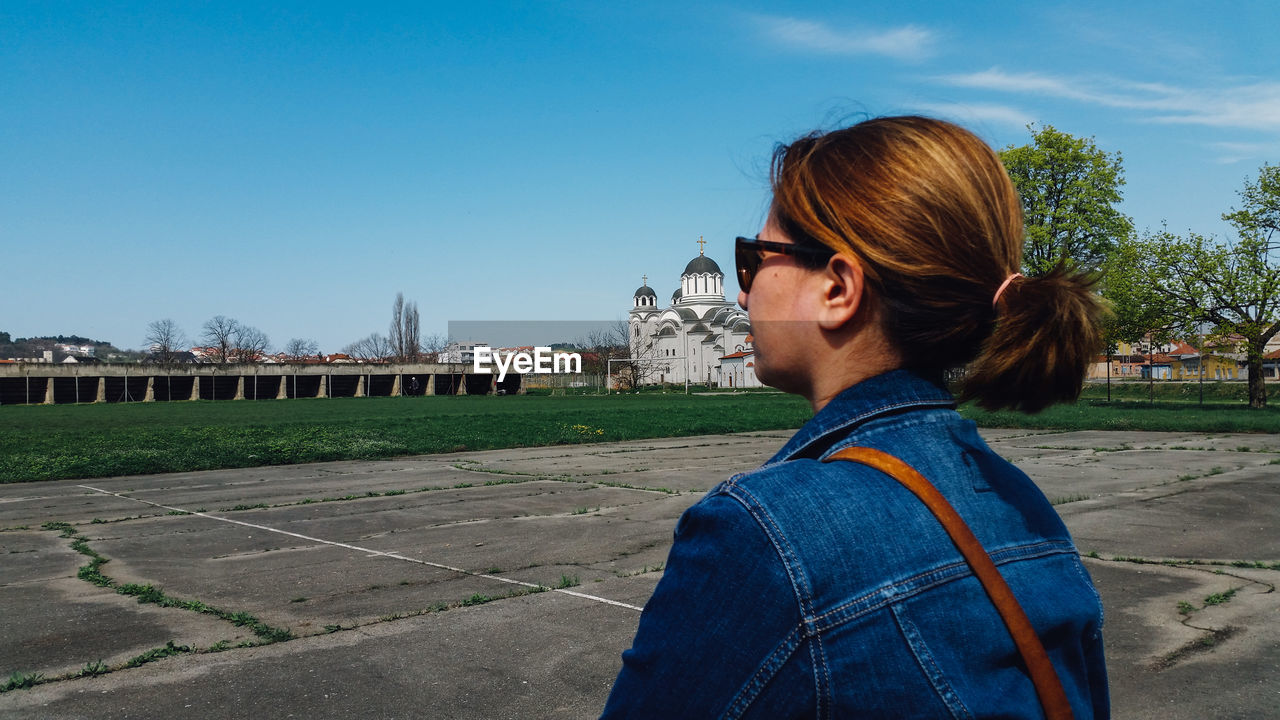 Woman looking at blue sky while standing by sport court