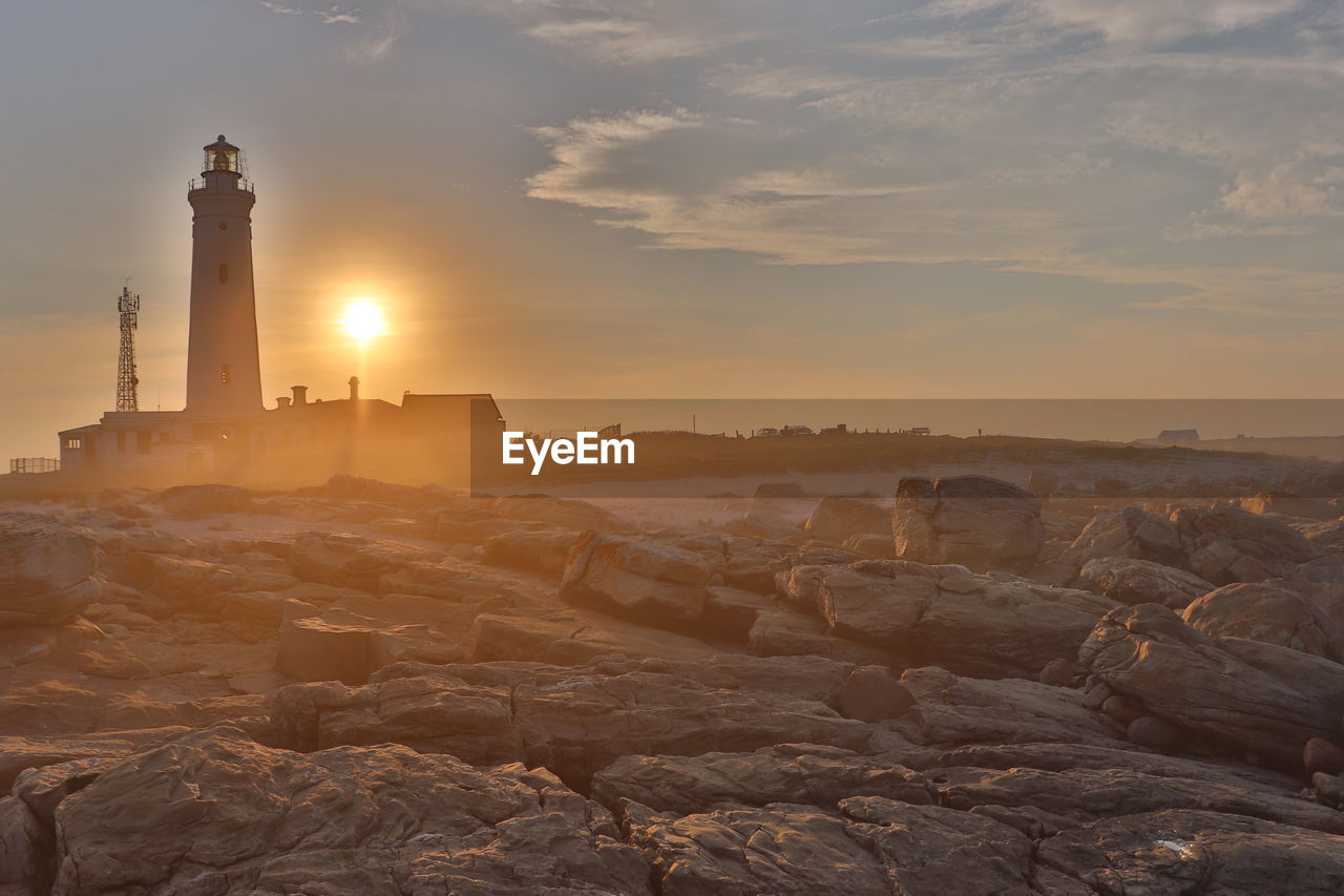 Lighthouse by sea against sky during sunset