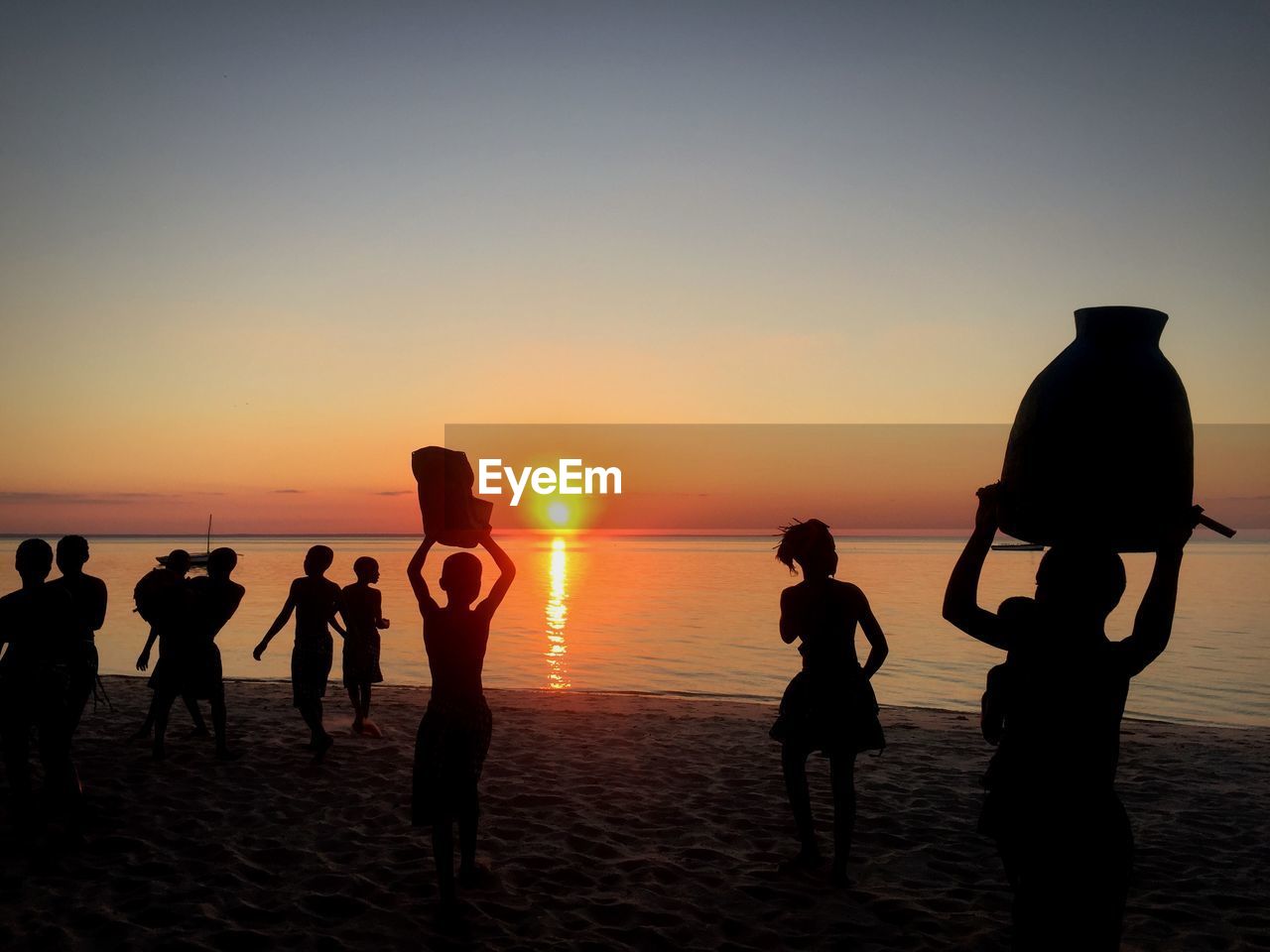 Silhouette people on beach against sky during sunset