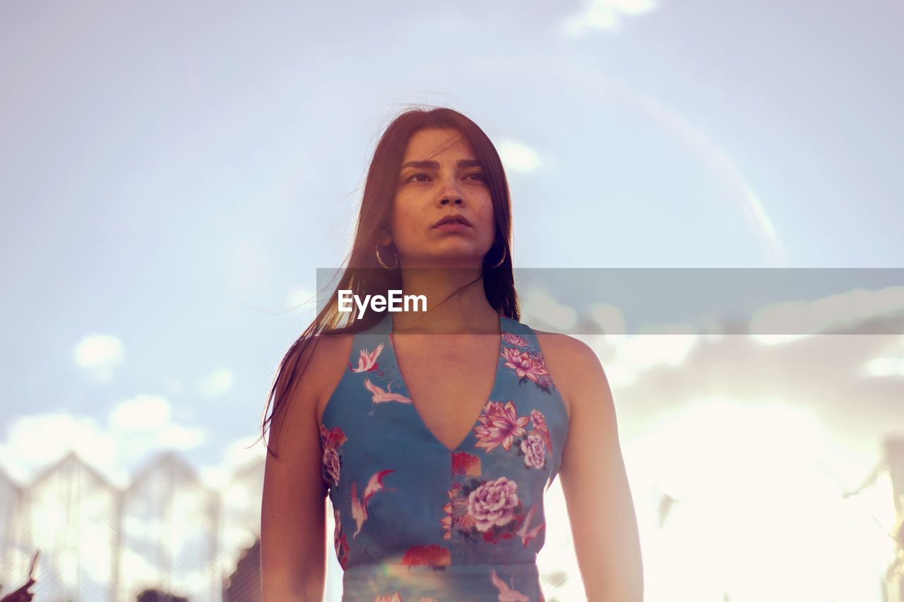 Low angle view of thoughtful young woman standing against sky