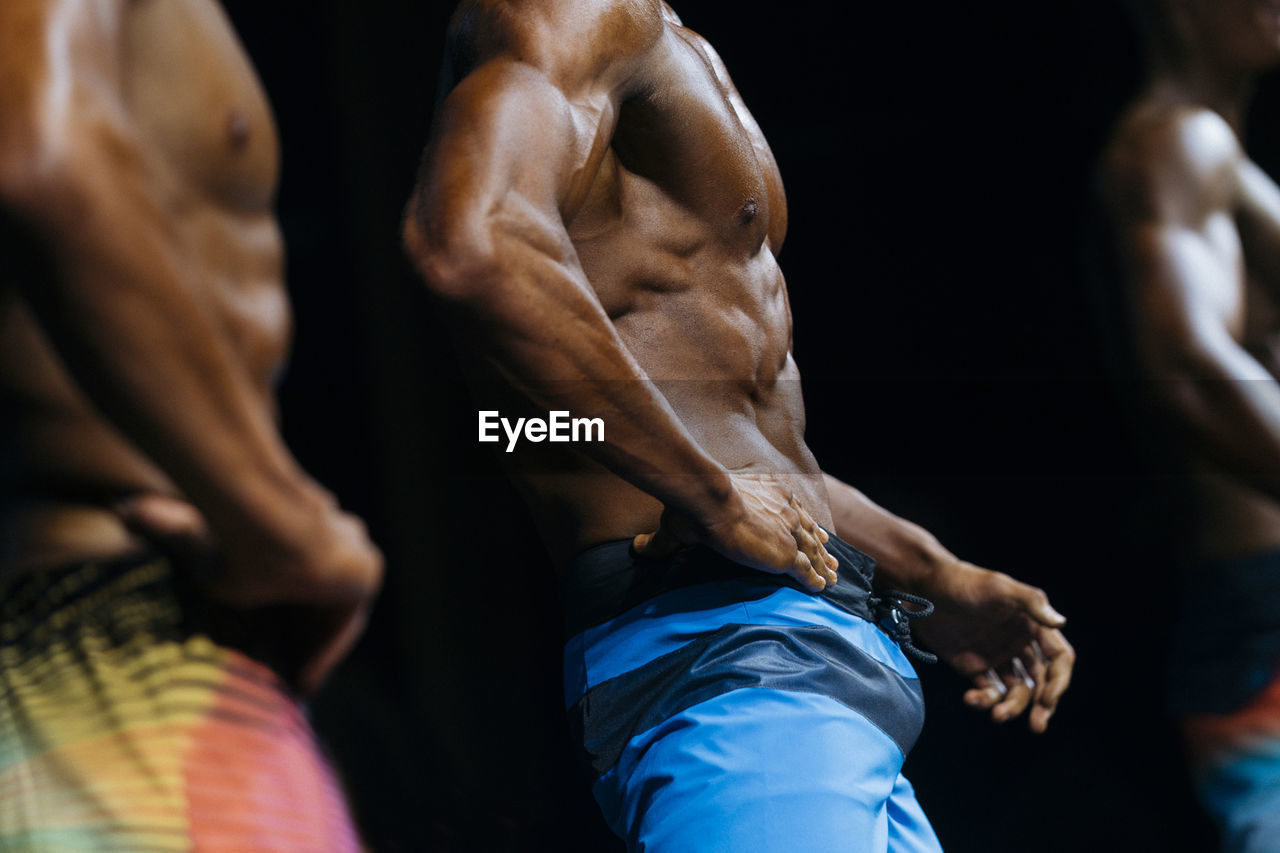 Midsection of shirtless athletes against black background