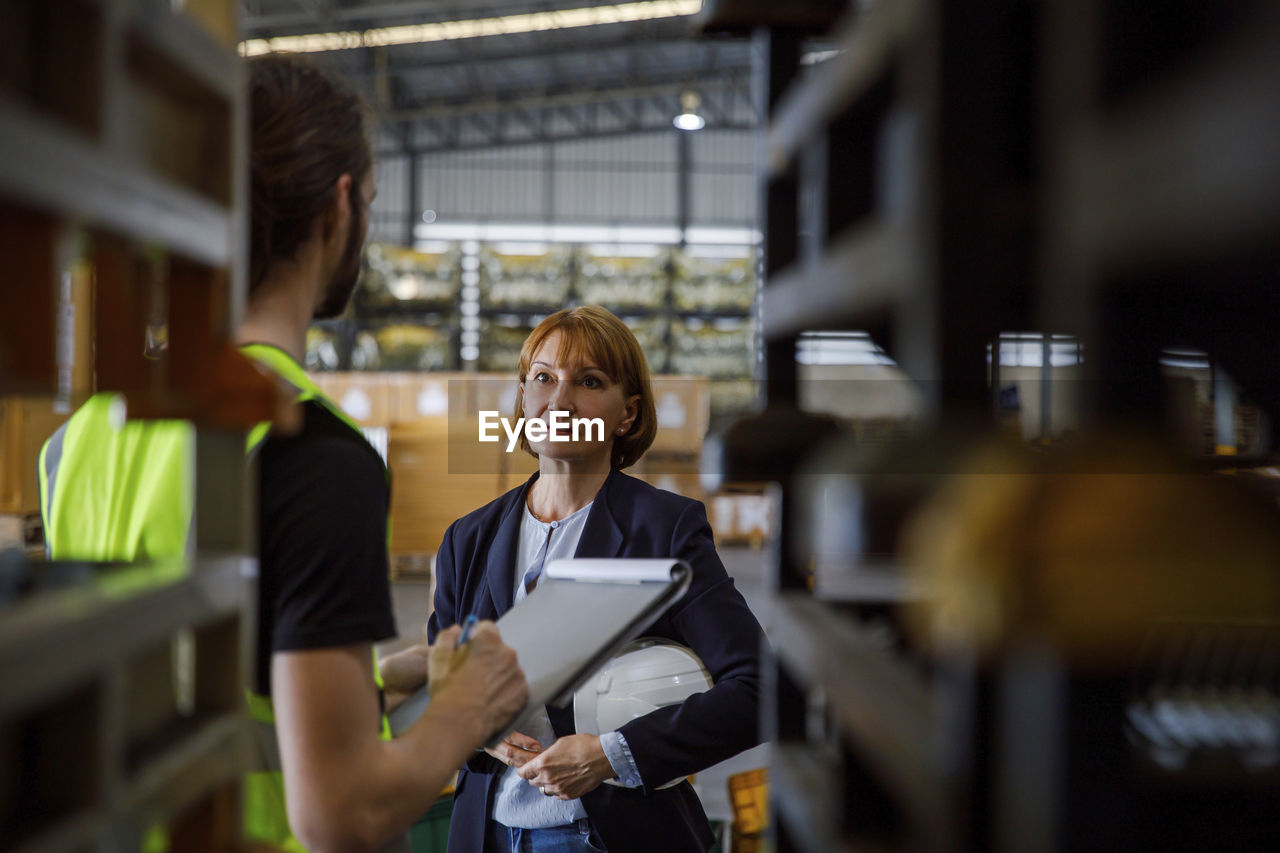 Manager with colleague checking with checklist at warehouse