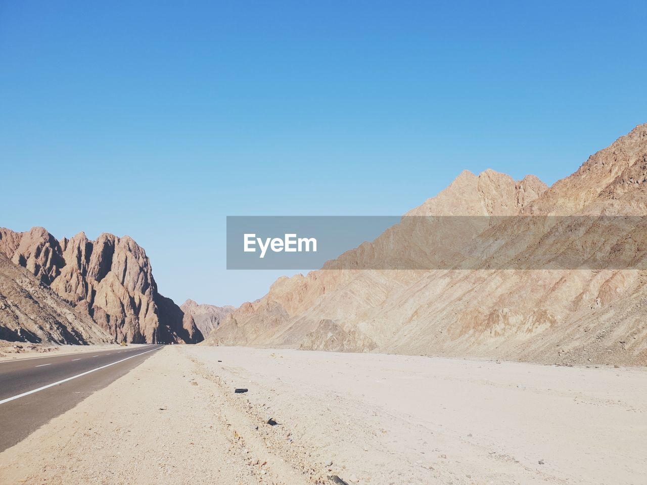 Scenic view of desert road against clear blue sky