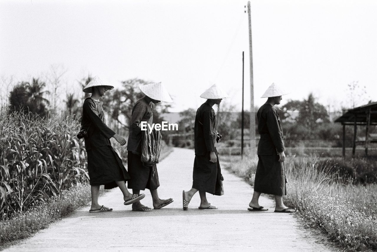 Side view of men wearing asian style conical hats while walking on road against clear sky