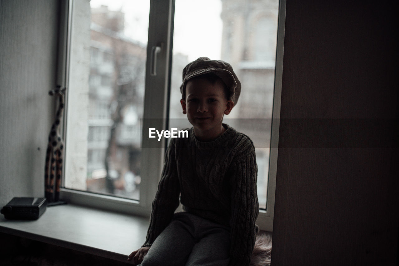 Portrait of boy standing by window at home