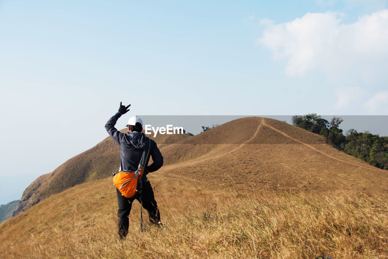 Rear view of hiker standing on mountain against sky