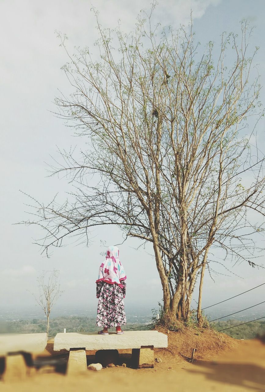 Girl standing on seat against bare trees