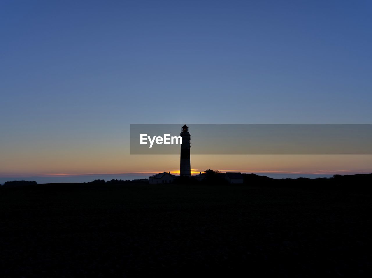 LIGHTHOUSE ON SILHOUETTE OF BUILDING AGAINST SKY DURING SUNSET