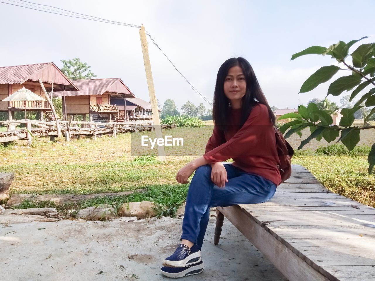 PORTRAIT OF SMILING YOUNG WOMAN SITTING ON PLANT