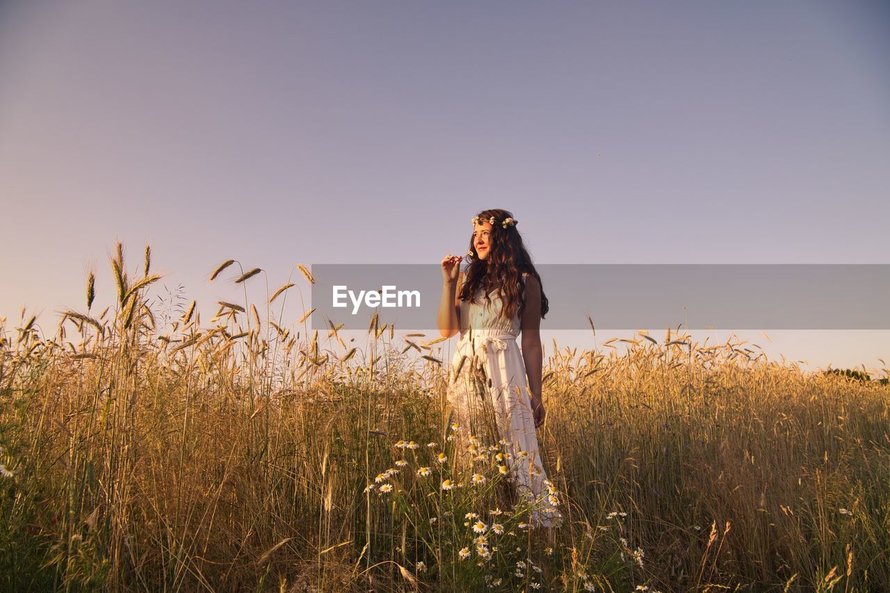 Young woman standing amidst plants against clear sky at sunset