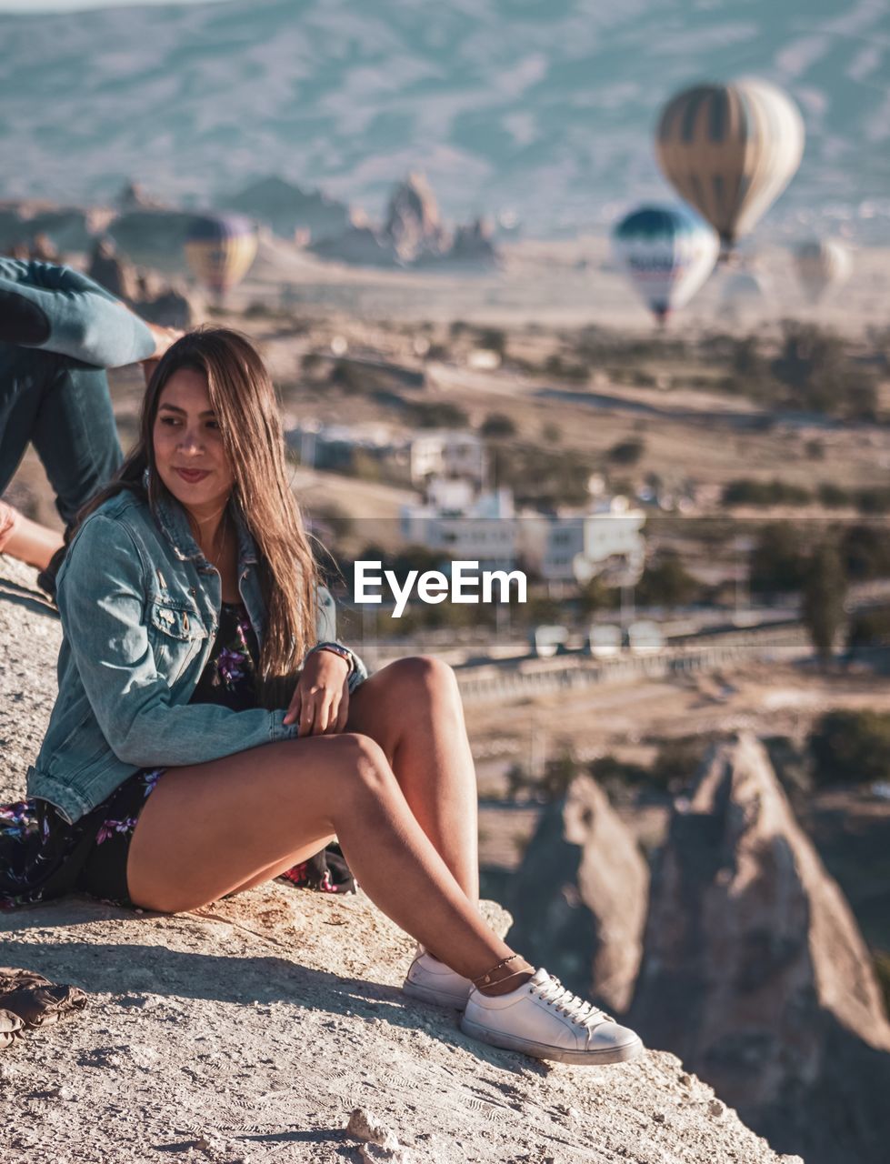 PORTRAIT OF SMILING WOMAN SITTING ON ROCK