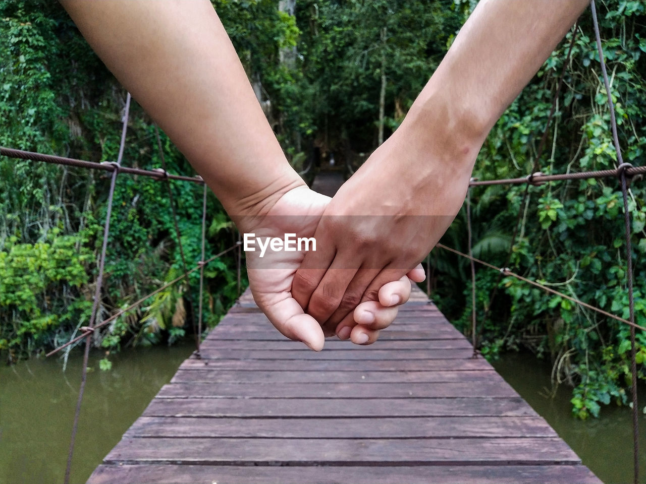 Cropped image of couple holding hands on footbridge