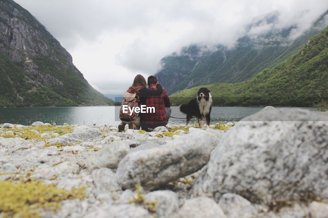 People crouching by dog against mountain