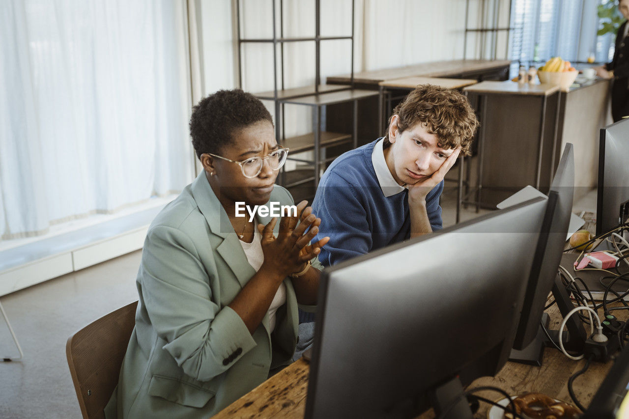Tensed multiracial male and female programmers looking at computer monitor in creative office