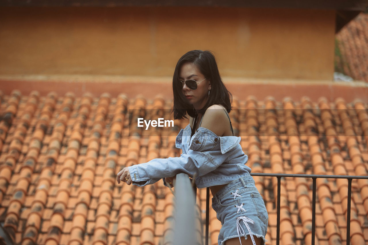Fashionable woman in sunglasses standing against roof tiles