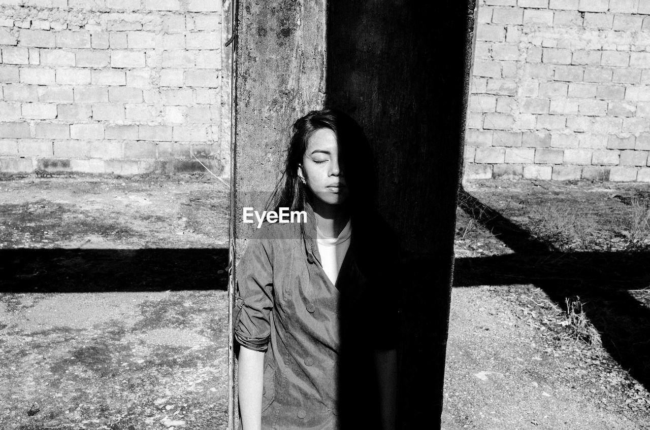 Young woman with eyes closed standing by concrete wall