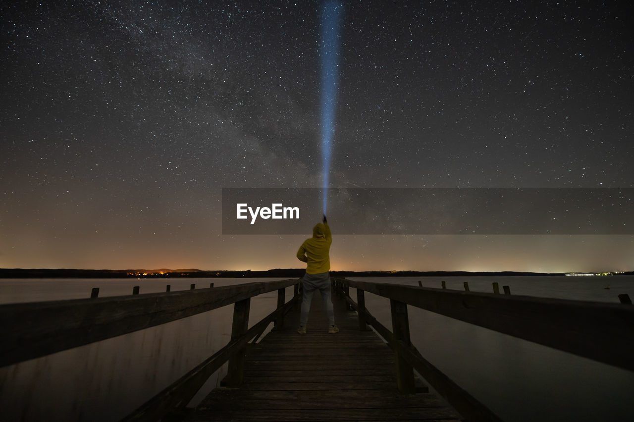 Rear view of man standing on pier against sky at night