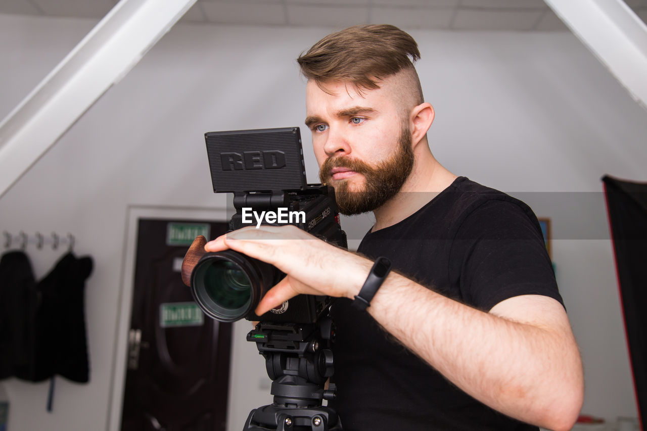 one person, adult, technology, beard, occupation, men, filmmaking, indoors, facial hair, arts culture and entertainment, young adult, camera, film industry, studio, working, filming, expertise, business, waist up, creativity, professional occupation, communication, looking, portrait, equipment
